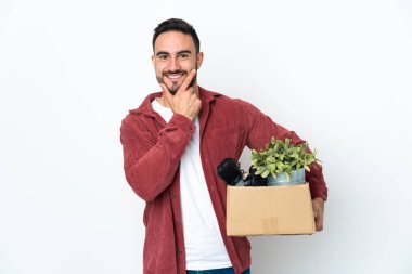 Beyaz arka planda izole olmuş mutlu ve gülümseyen şeylerle dolu bir kutuyu alırken genç beyaz bir adam hamle yapıyor.
