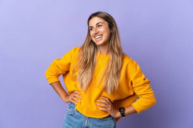 Kolları kalçasında poz veren ve gülümseyen, soyutlanmış mor bir geçmişi olan genç İspanyol kadın.