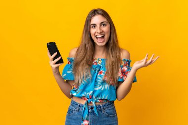 İzole edilmiş sarı arka planda cep telefonu kullanan genç bir kadın.