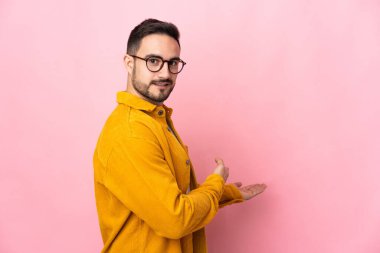Pembe arka planda soyutlanmış beyaz tenli yakışıklı adam davet edildiği için ellerini yana uzatıyor.