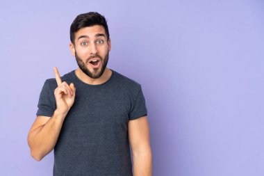 Kafkasyalı yakışıklı adam çözümü kavramak için parmağını izole edilmiş mor arka plan üzerine kaldırıyor.