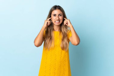 İzole edilmiş mavi arka planda genç İspanyol kadın hayal kırıklığına uğramış ve kulaklarını kapatmış.
