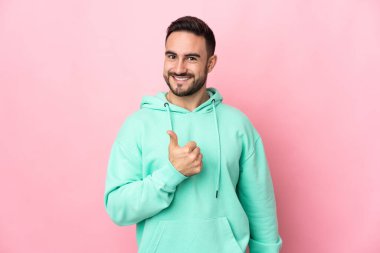 Pembe arka planda izole edilmiş beyaz, yakışıklı bir genç baş parmak hareketi yapıyor.