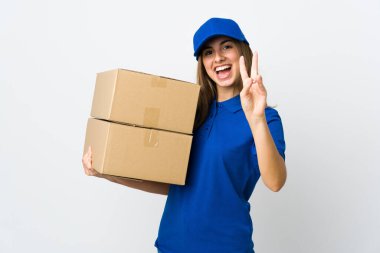 İzole edilmiş beyaz arka planda genç teslimatçı kadın gülümsüyor ve zafer işareti gösteriyor.