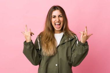 Soyutlanmış pembe arka planda genç bir kadın boynuz hareketi yapıyor.