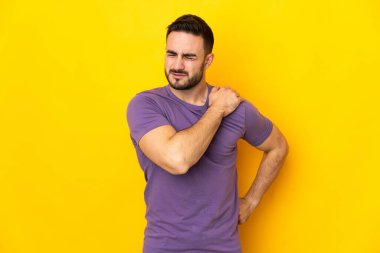 Beyaz tenli yakışıklı, sarı arka planda izole edilmiş, omuz ağrısından muzdarip, çaba sarf ettiği için.