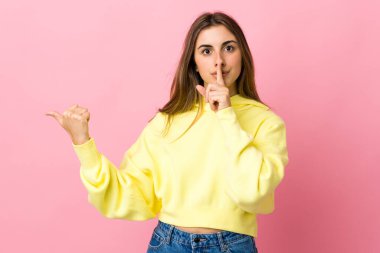 Soyutlanmış pembe arka planda genç bir kadın yan tarafı işaret ediyor ve sessiz hareketler yapıyor.