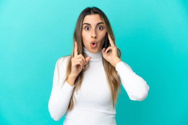 Mavi arka planda izole edilmiş cep telefonu kullanan beyaz bir kadın çözümü bulmak için parmağını kaldırıyor.