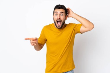 Beyaz arka planda sakallı yakışıklı genç adam şaşırdı ve parmağını yana uzattı.