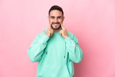 Beyaz tenli yakışıklı adam pembe arka planda izole edilmiş mutlu ve hoş bir ifadeyle gülümsüyor.