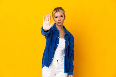 Sarı arka planda izole edilmiş genç Rus kadın dur hareketi yapıyor.