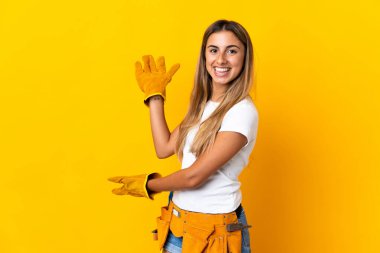 Genç İspanyol elektrikçi kadın, izole edilmiş sarı duvarın üzerinden elini uzatarak davet ediyor.