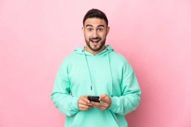 Pembe arka planda izole edilmiş beyaz, yakışıklı genç bir adam şaşırdı ve bir mesaj gönderiyor.