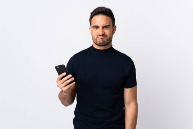 Beyaz arka planda izole edilmiş, üzgün bir ifadeyle cep telefonu kullanan beyaz bir adam.