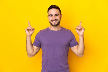 Sarı arka planda izole edilmiş beyaz, yakışıklı genç adam harika bir fikre işaret ediyor.