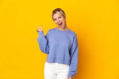 Sarı arka planda izole edilmiş genç Rus kadın gülümsüyor ve zafer işareti gösteriyor.