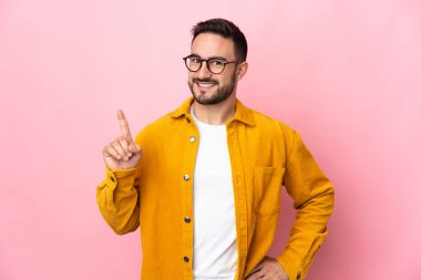 Pembe arka planda izole edilmiş beyaz, yakışıklı genç bir adam en iyinin işareti olarak parmağını kaldırıyor.