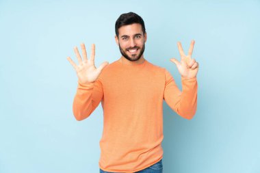 Kafkasyalı yakışıklı adam, izole edilmiş mavi arka planda parmakları olan sekiz kişi sayıyor.