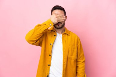 Beyaz tenli yakışıklı adam pembe arka planda izole edilmiş gözlerini elleriyle kapatıyor. Bir şey görmek istemiyorum.
