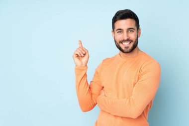 Kafkas yakışıklı adam mutlu ve izole edilmiş mavi arka plan üzerinde işaret ediyor.