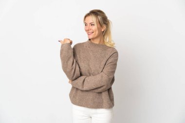 Beyaz arka planda izole edilmiş genç Rus kadın bir ürünü sunmak için kenarı işaret ediyor.