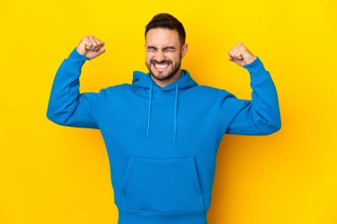 Sarı arka planda izole edilmiş beyaz, yakışıklı genç adam güçlü bir jest yapıyor.