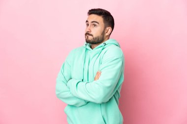 Beyaz tenli yakışıklı adam pembe arka planda izole edilmiş. Omuzlarını kaldırırken şüpheyle hareket ediyor.