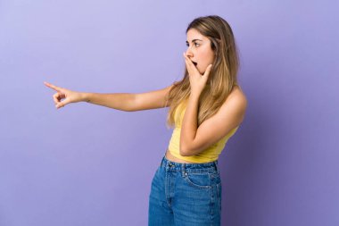 İzole edilmiş mor arka planı olan genç bir kadın sürpriz bir ifadeyle işaret ederken...