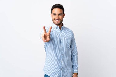 Genç ve yakışıklı bir adam izole edilmiş arka planda gülümsüyor ve zafer işareti gösteriyor