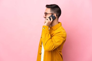 Beyaz tenli yakışıklı adam pembe arka planda izole edilmiş cep telefonuyla sohbet ediyor.