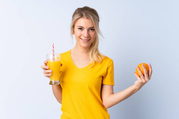 Blonde woman over isolated blue background holding an orange and an orange juice