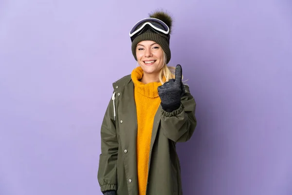 俄罗斯滑雪者女孩带着雪板眼镜与紫色背景隔离来做手势 — 图库照片