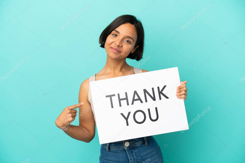 Young mixed race woman isolated on blue background holding a placard with text THANK YOU and  pointing it