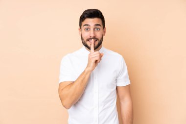Beyaz tenli yakışıklı adam bej arka planda izole edilmiş. Parmağını ağzına koyduğunda sessizlik işareti gösteriyor.