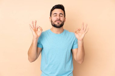 Beyaz tenli yakışıklı adam, bej arka planda Zen pozuyla izole edilmiş.