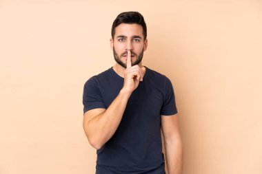 Beyaz tenli yakışıklı adam bej arka planda izole edilmiş. Parmağını ağzına koyduğunda sessizlik işareti gösteriyor.