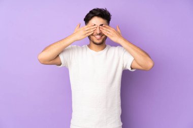 İzole edilmiş arka planda yaşayan yakışıklı Arap bir adam. Gözleri elleriyle kaplıyor ve gülümsüyor.