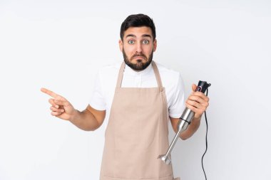 Beyaz arkaplanda izole edilmiş el blenderi kullanan adam, yan taraftaki şüpheleri işaret ediyor.