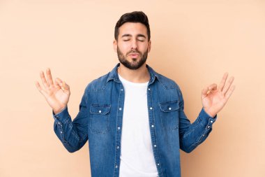 Beyaz tenli yakışıklı adam, bej arka planda Zen pozuyla izole edilmiş.