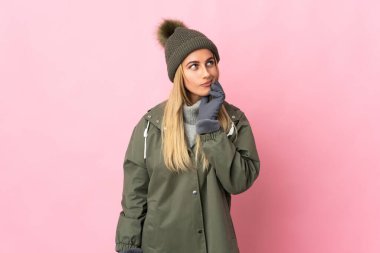 Pembe arka planda izole edilmiş, kış şapkalı genç bir kadının şüpheleri ve düşünceleri var.