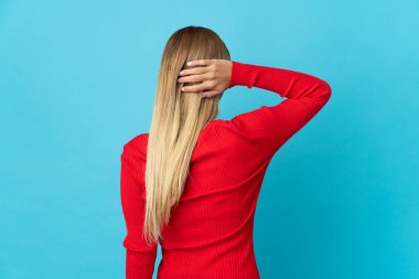 Genç sarışın kadın mavi arka planda izole edilmiş ve düşünüyor.