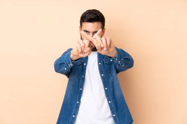 Beyaz tenli yakışıklı adam bej arka planda izole edilmiş bir şekilde bir eylemi durdurmak için el hareketi yapıyor.