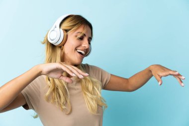 Genç sarışın Uruguaylı, mavi arka planda izole edilmiş müzik ve dans dinliyor.