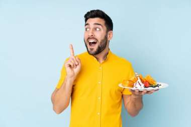 Beyaz adam mavi arka planda izole edilmiş waffle 'lar tutuyor. Çözümü bulmak için parmağını kaldırıyor.