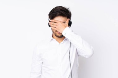 Tele pazarlamacı Arap adam kulaklıkla çalışıyor. Beyaz arka planda izole edilmiş, gözleri elle kapatıyor.