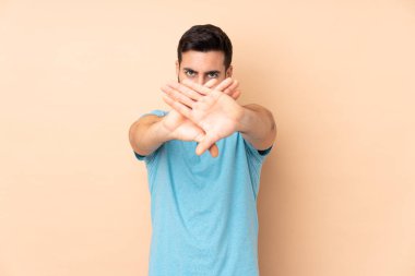 Beyaz tenli yakışıklı adam bej arka planda izole edilmiş bir şekilde bir eylemi durdurmak için el hareketi yapıyor.
