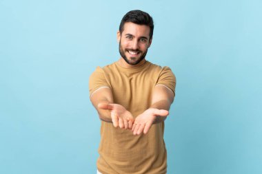 Arka planı izole edilmiş sakallı genç yakışıklı bir adam bir ilan vermek için avucunda hayali bir şey tutuyor.