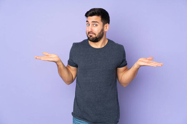 Caucasian handsome man having doubts while raising hands over isolated purple background