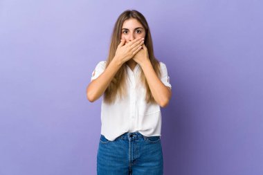 İzole edilmiş mor arka planı olan genç bir kadın elleriyle ağzını kapatıyor.