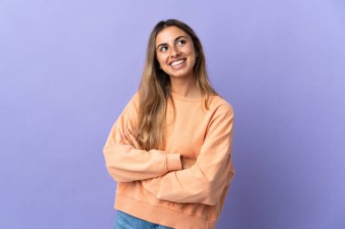 İzole edilmiş mor arka planı olan genç İspanyol kadın gülümserken yukarı bakıyor.